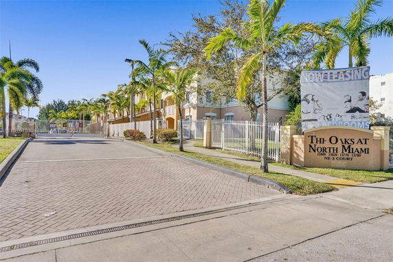 Front view of a gated residential complex with palm trees and a sign.