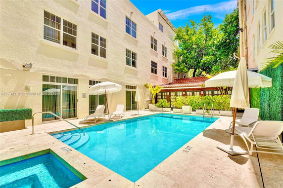 Outdoor swimming pool area with lounge chairs and umbrellas next to a multi-story building.