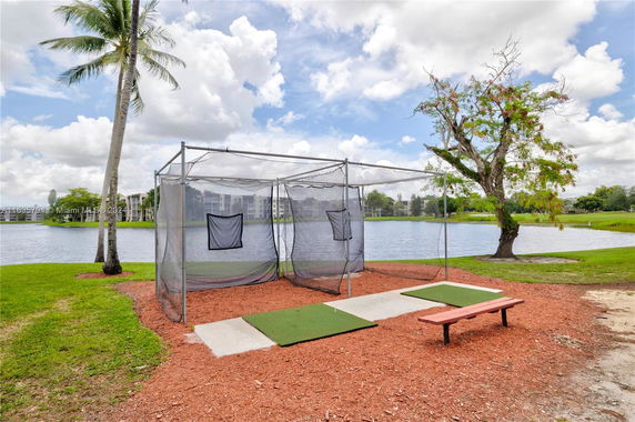 Outdoor batting cage near a lake with palm trees.