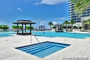 Outdoor view of a swimming pool area with lounge spaces and a tall building in the background.