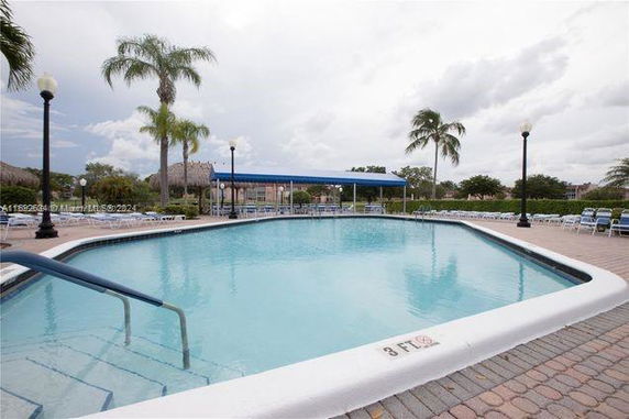 Outdoor swimming pool with surrounding chairs and palm trees.
