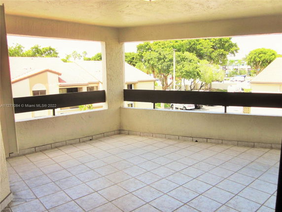 Concrete balcony view from a building towards surrounding residential area with other buildings and trees.
