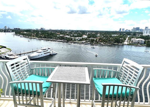 View from a balcony overlooking a river with boats and distant city skyline.
