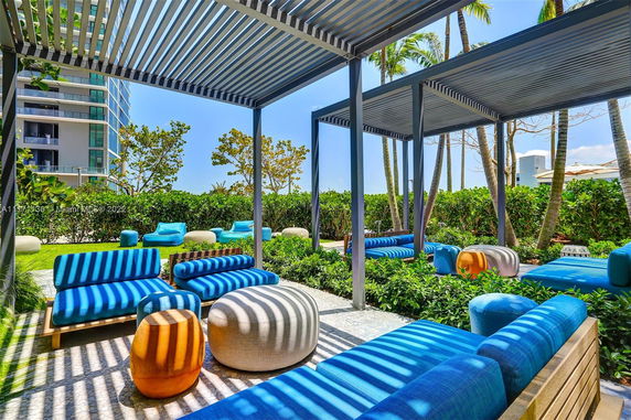 Outdoor seating area with blue and beige cushions and a lattice pergola, adjacent to a building.