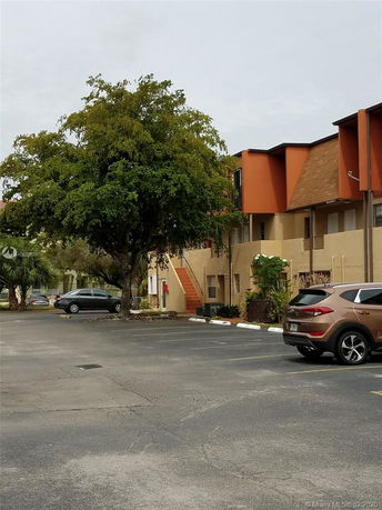 Outdoor parking area in front of a multi-story building with orange accents.