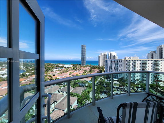 Panoramic view from a balcony overlooking urban and coastal scenery with tall buildings and the ocean in the distance.