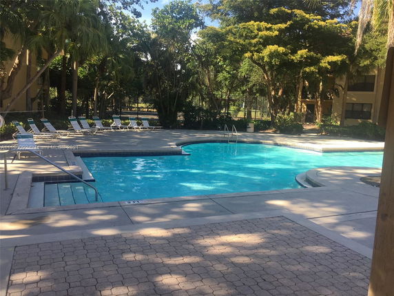 Outdoor swimming pool area with lounge chairs and trees in the background.
