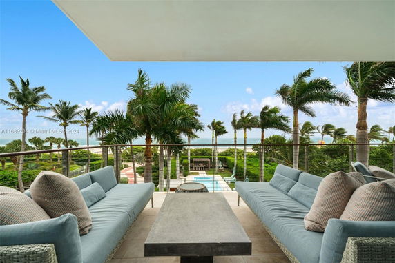 Outdoor seating area with ocean view, palm trees, and blue sky.