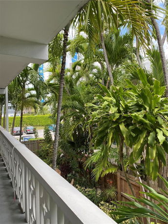 Balcony view overlooking tropical plants and parked cars in a residential area.