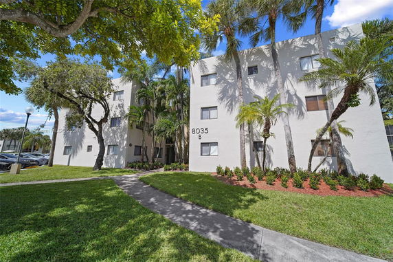 Front view of a multi-story building with a white facade and surrounding palm trees.