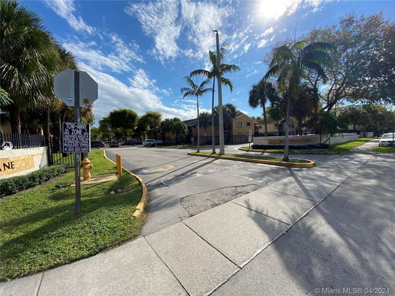 Street view of residential area with palm trees and a gated entrance.