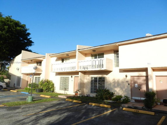 Front view of a two-story apartment building with balconies and parking spaces.