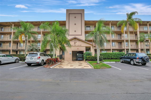 Front view of a multi-story residential building with balconies and a parking area.