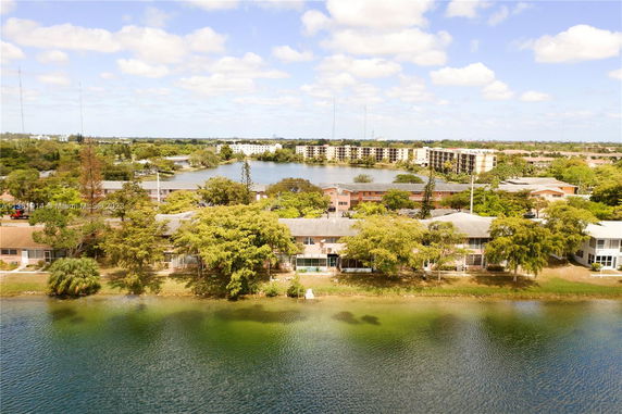 Aerial view showing residential buildings surrounded by trees and a body of water.