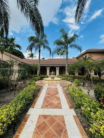 Front view of a house with a central walkway and fountain, surrounded by palm trees.