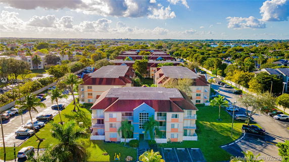 Aerial view of multiple residential buildings with red roofs surrounded by greenery and parking areas.