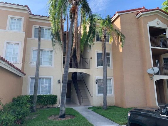 Front view of a multi-story residential building with a staircase and palm trees.