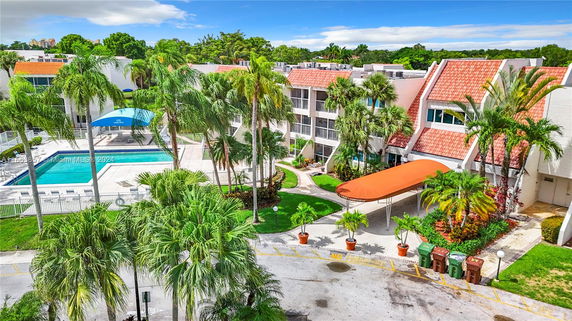 Outdoor view of a building complex with a swimming pool surrounded by palm trees.
