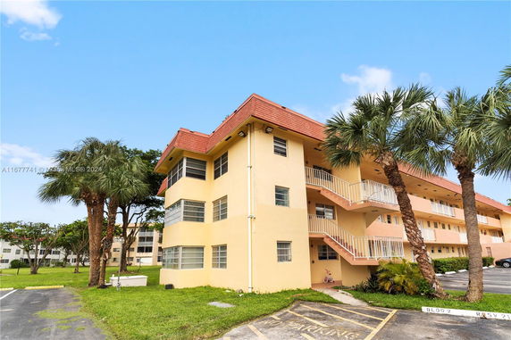 Front view of a three-story apartment building with an external staircase and palm trees nearby.