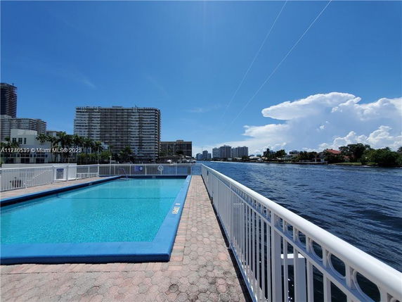 Outdoor swimming pool with surrounding buildings near a waterfront.