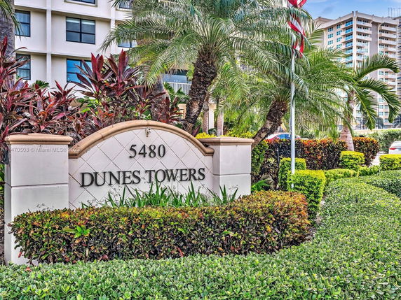 Exterior view of a multi-story building with landscaped entrance marked by 'Dunes Towers.'