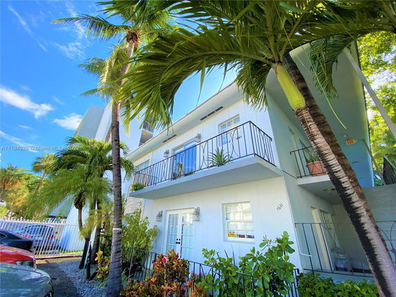 Front view of a multi-story building with balconies and tropical plants.