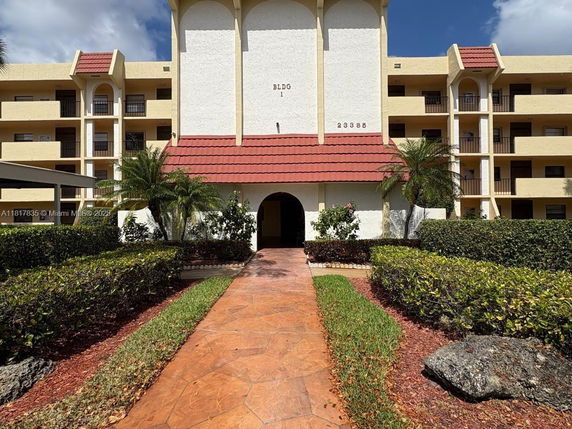 Front view of a multi-story building with arches and red roofing over the entrance.