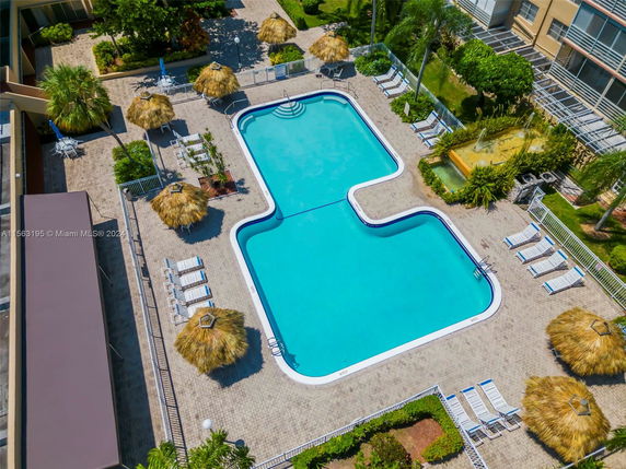 Aerial view of an outdoor swimming pool area with lounge chairs and thatched umbrellas.