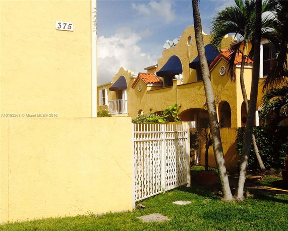 Front view of a house with yellow stucco walls and blue awnings.