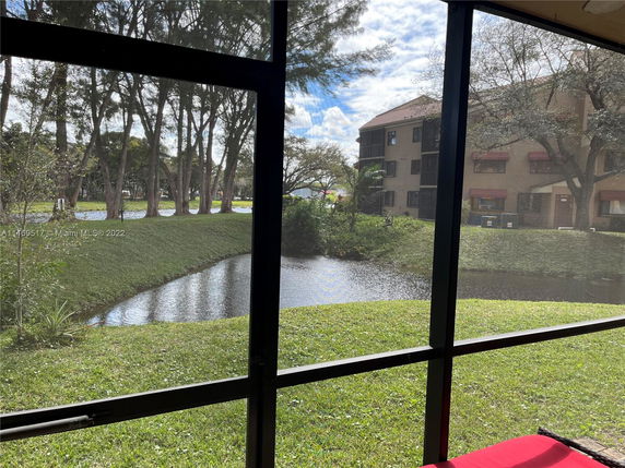 View through a window showing a pond, grassy area, and trees with a building in the background.