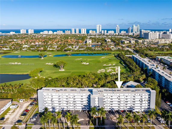Aerial view of a residential building with a golf course and cityscape in the background.