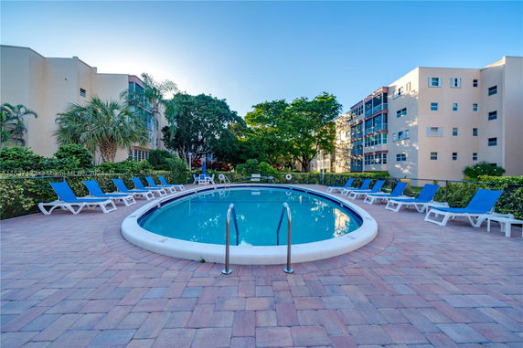 Outdoor swimming pool surrounded by lounge chairs and apartment buildings.