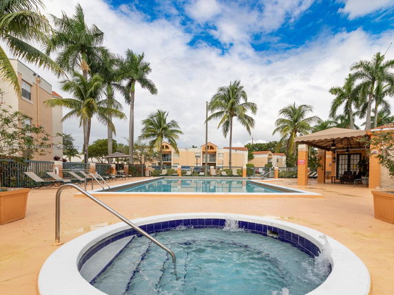 Outdoor swimming pool area with palm trees and seating.