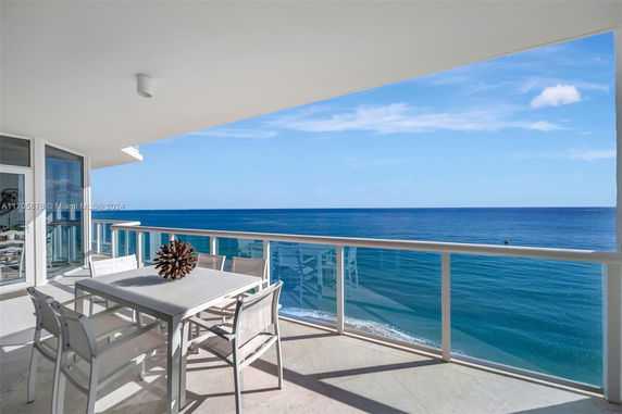 Balcony view of the ocean with a dining table and chairs.