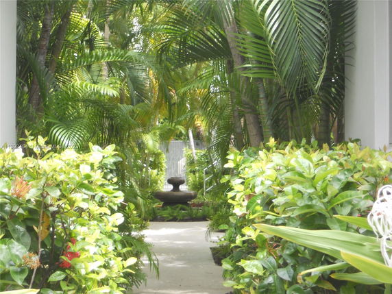 Outdoor pathway surrounded by lush green plants and a water fountain.