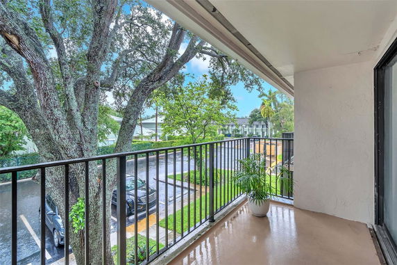 Balcony view showing trees, a parking area, and nearby buildings.