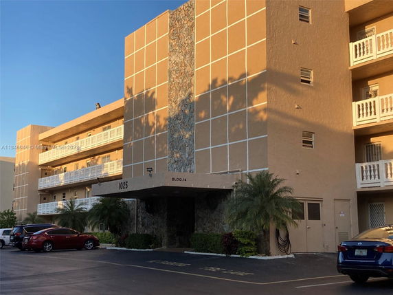 Front view of a multi-story building with balconies and a parking area.
