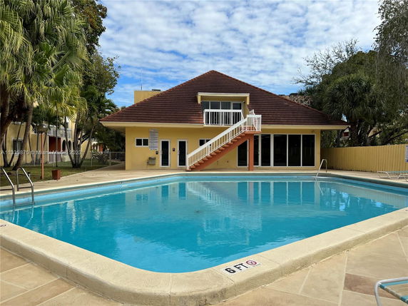 Outdoor swimming pool area with a two-story building nearby.