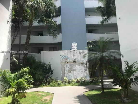 Front view of a multi-story building with balconies and palm trees in the foreground.