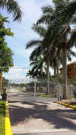 Entrance gate with palm trees and a two-story building nearby.