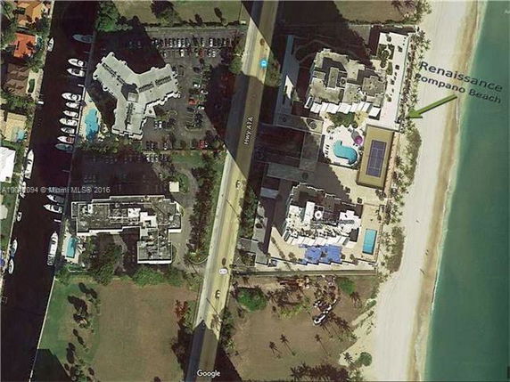 Aerial view of a beachfront building complex with visible rooftops featuring a pool and solar panels.