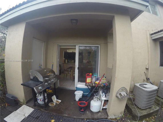 View of a small patio area with a barbecue grill, an air conditioning unit, and sliding glass doors leading inside.