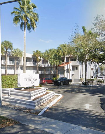 Front view of a multi-story residential building with balconies and a sign at the entrance.