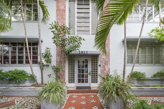 Front elevation view of a building with a glass panel door and decorative plants.