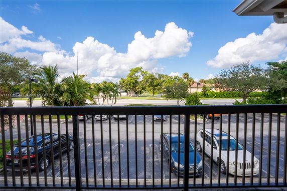 View from a balcony overlooking a parking area with several cars and trees in the distance.