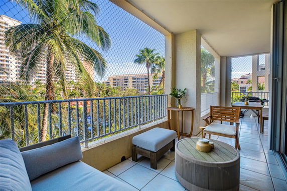 Balcony view with seating furniture overlooking nearby buildings and palm trees.