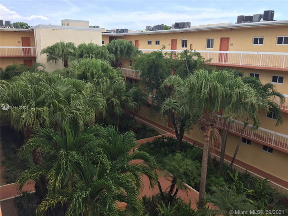View of a multi-story building with yellow exteriors, surrounded by lush greenery.