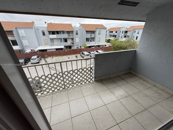 View of several residential buildings with balconies and red-tiled roofs, seen from a tiled balcony.