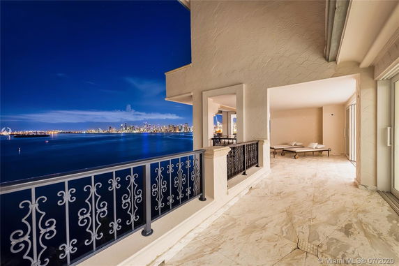 Balcony view with ornate railing overlooking a body of water and city skyline at night.