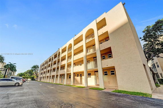 Front view of a multi-story apartment building with balconies and parking area.
